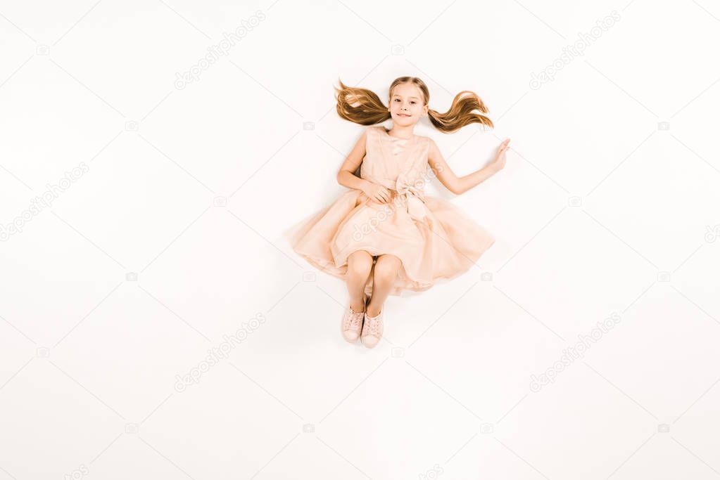 top view of smiling kid in dress looking at camera on white