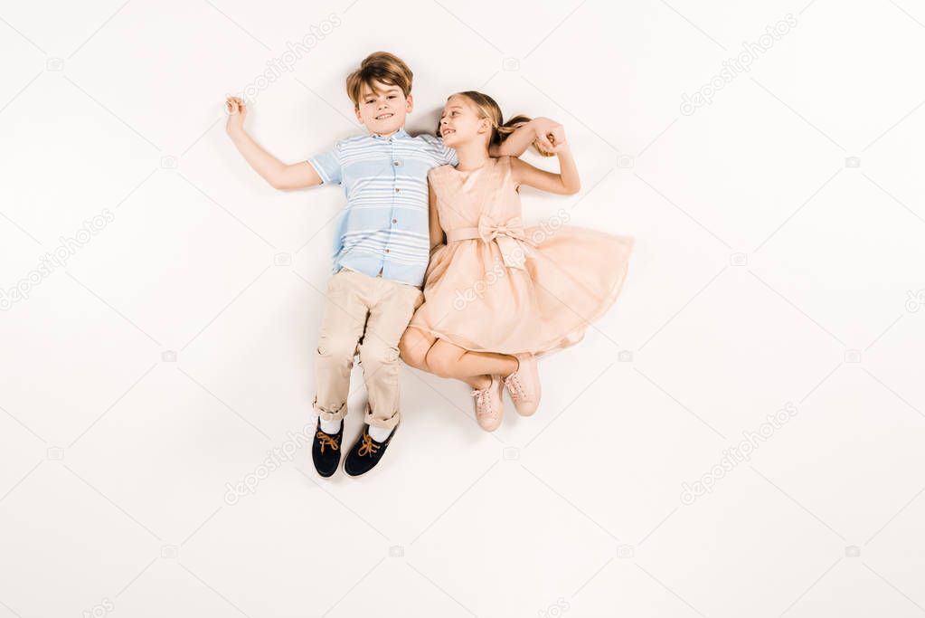 top view of cheerful kid in pink dress holding hands with friend on white 