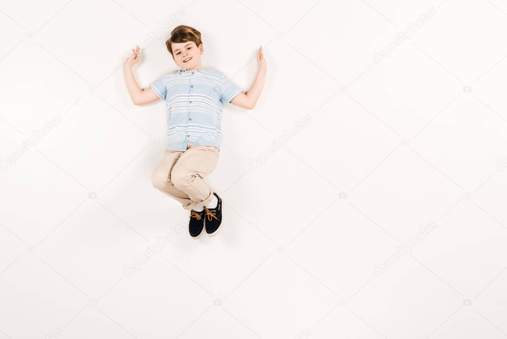 top view of happy kid looking at camera while lying on white 
