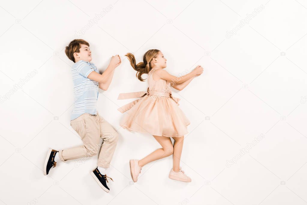 top view of cheerful kids gesturing while lying on white 