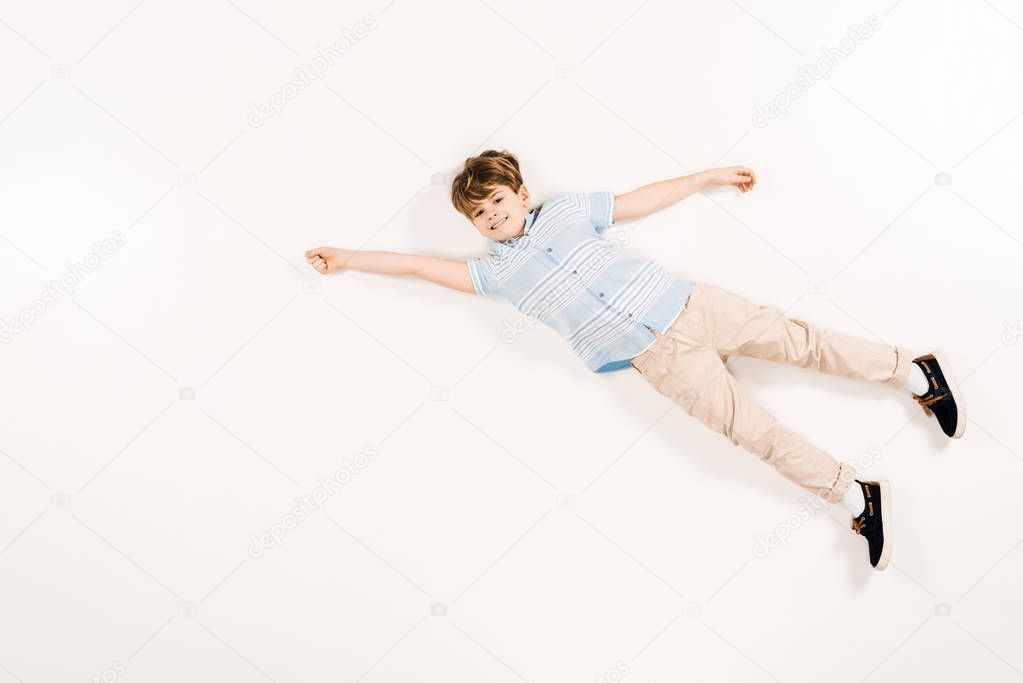 happy child looking at camera and gesturing while lying on white 