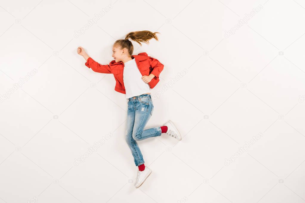 top view of happy kid in jeans gesturing while lying on white 