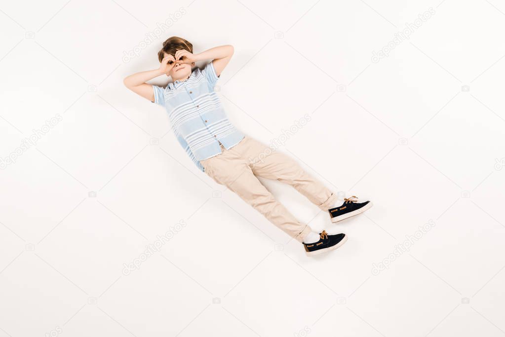 cute kid with hands near eyes lying on white 