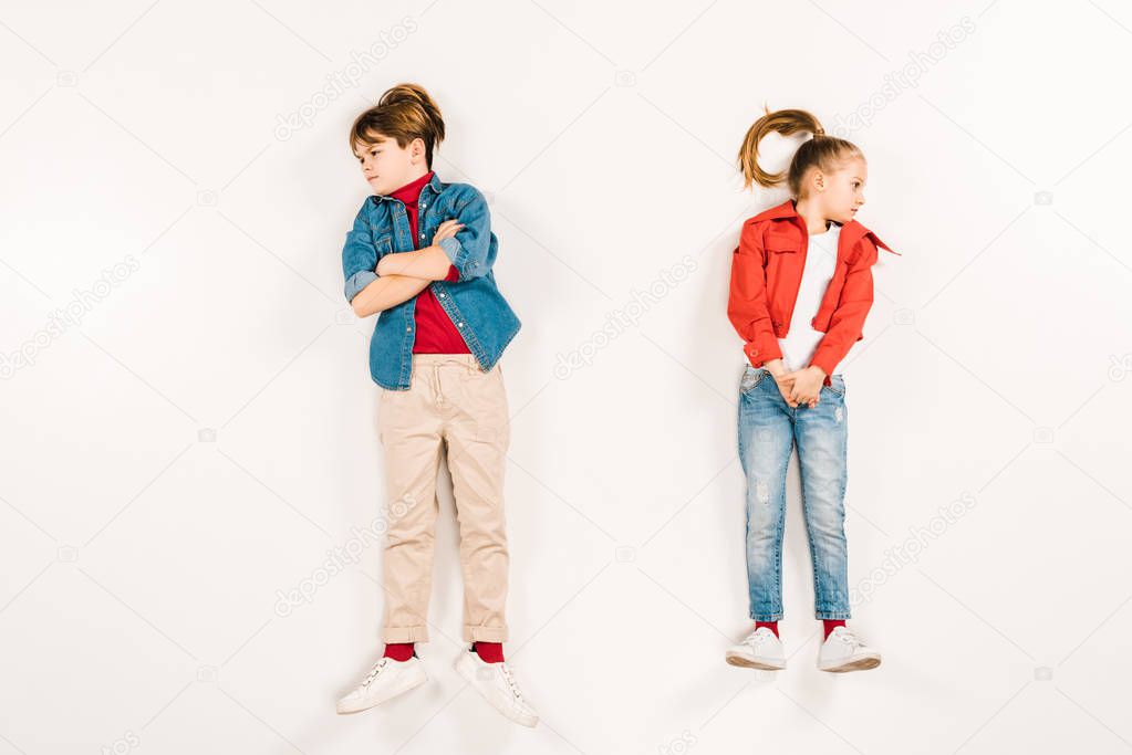 top view of displeased kid with crossed arms near friend on white 