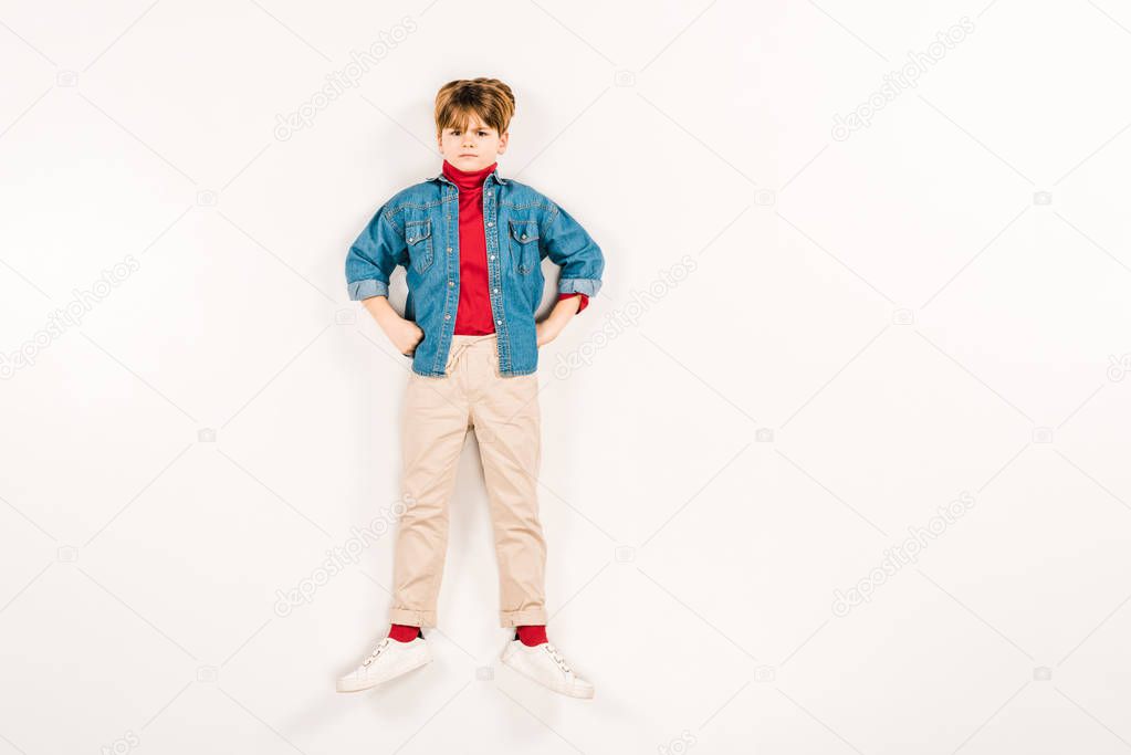 top view of upset kid with hands on hips lying on white 