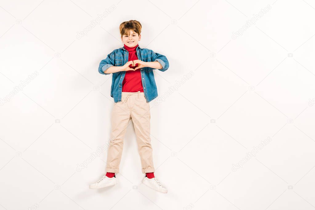 top view of cheerful child showing heart-shape sign on white 