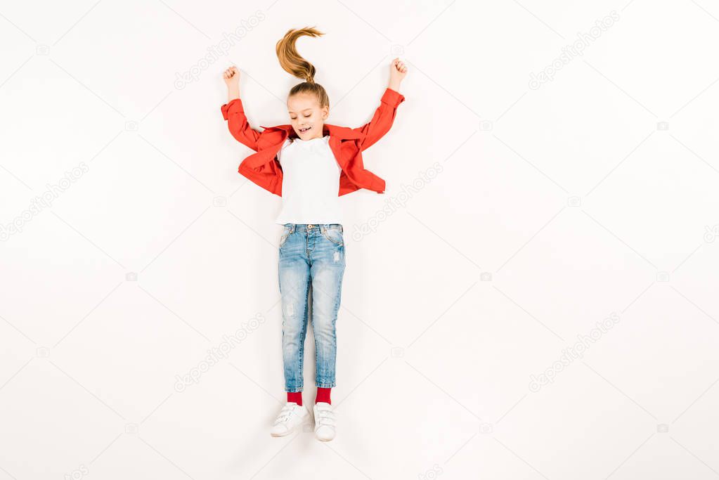 top view of happy child with hands above head smiling on white 