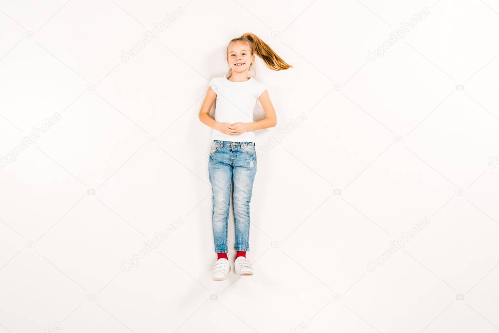 top view of happy kid with clenched hands lying on white 
