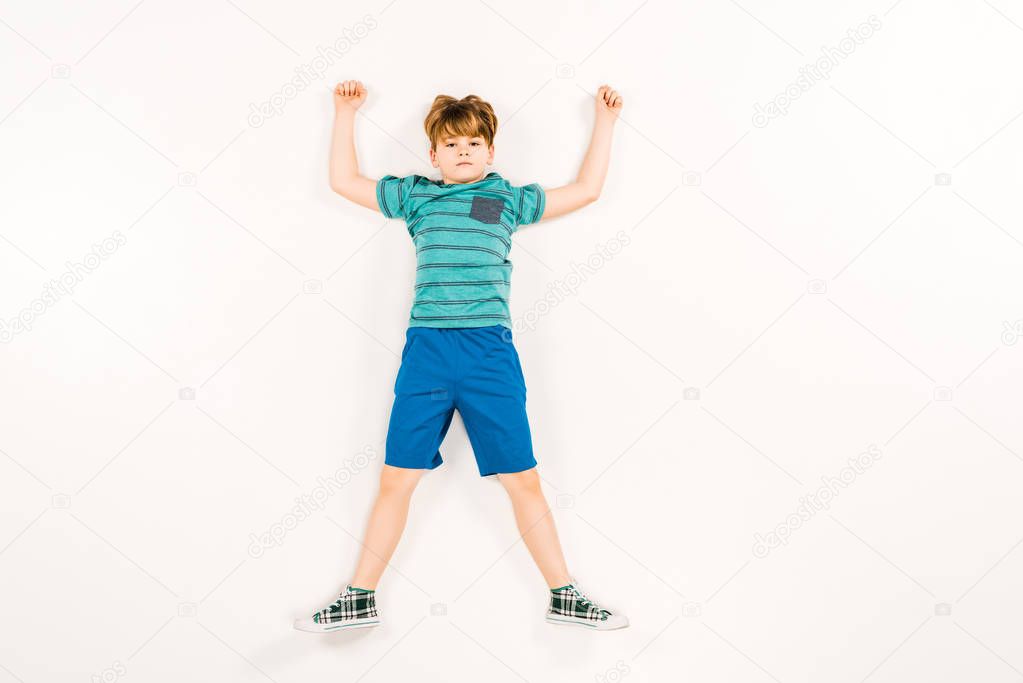 top view of cute kid with hands above head looking at camera on white 