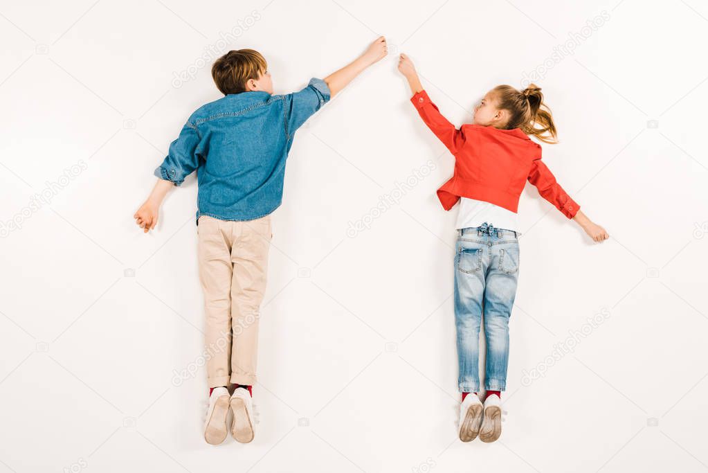 top view of cute kids gesturing while lying on white 