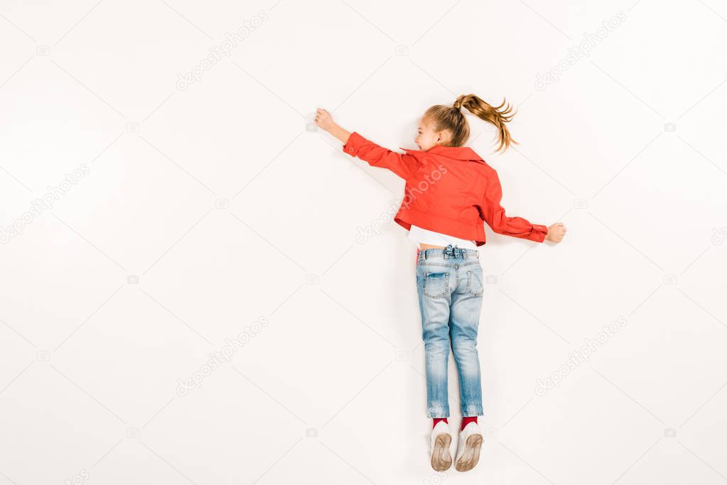 top view of happy kid in blue jeans gesturing while lying on white 