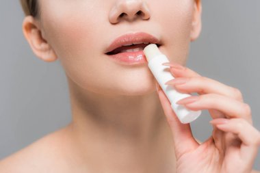 gri izole dudaklar yakınında dudak merhem tutan genç kadının kırpılmış görünümü 
