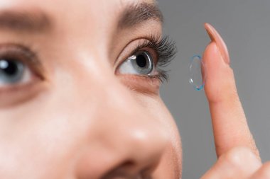 cropped view of young woman attaching contact lens isolated on grey clipart