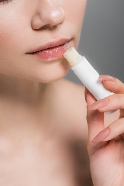cropped view of girl holding lip balm near lips isolated on grey  clipart