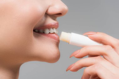 gri izole dudaklar yakınında dudak merhem tutan neşeli kız kırpılmış görünümü 