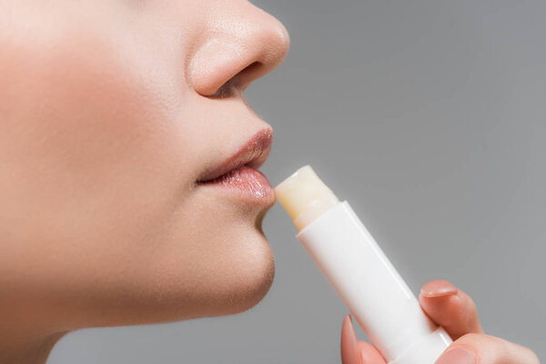 cropped view of woman holding lip balm isolated on grey 