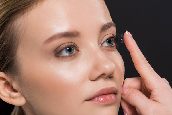 beautiful young woman attaching contact lens isolated on black 