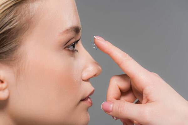 attractive girl attaching contact lens isolated on grey 