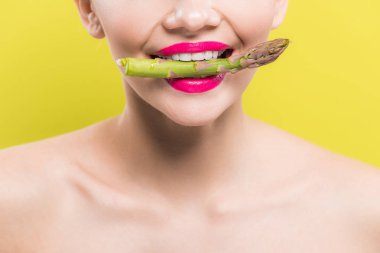 cropped view of cheerful naked woman holding green and tasty asparagus in mouth isolated on yellow  clipart