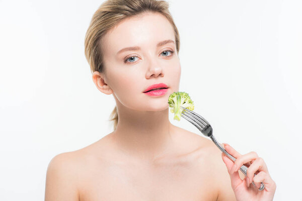 attractive naked woman holding silver fork with broccoli near pink lips isolated on white  