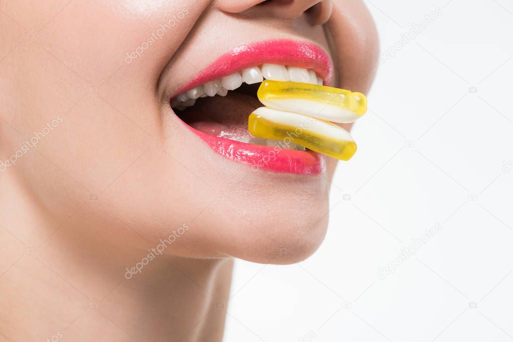 cropped view of cheerful girl eating yellow jelly candies isolated on white 