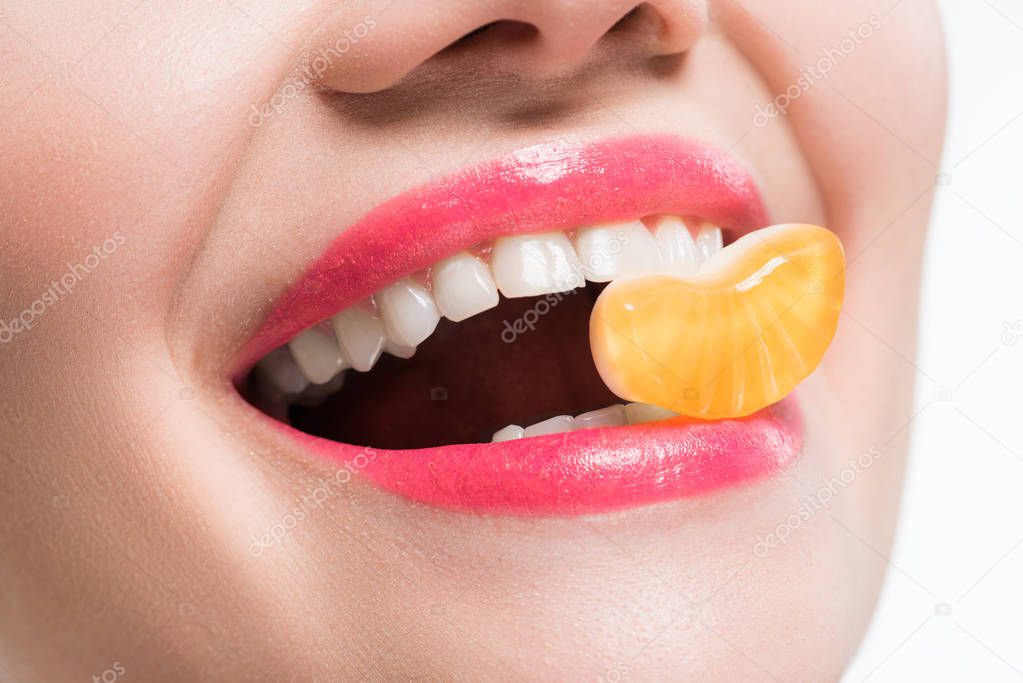 cropped view of smiling girl eating orange jelly candy isolated on white 