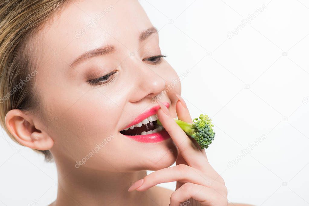 attractive and happy woman eating green ripe broccoli isolated on white   
