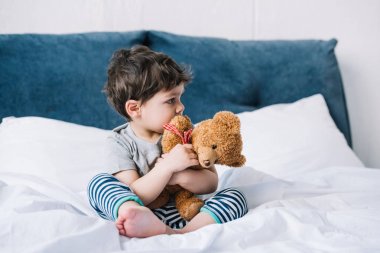 yalınayak yatakta oturan ve oyuncak ayı tutan sevimli çocuk 