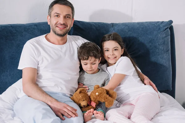 幸せな娘と悲しい幼児の息子とベッドに座って陽気な父親 — ストック写真