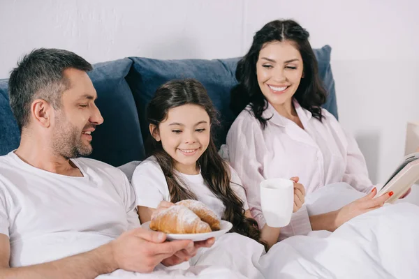 Cheerful Woman Holding Book Daughter Cup Husband Croissants — Stock Photo, Image