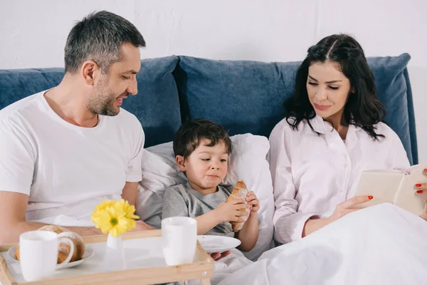 Glückliche Eltern Schauen Kleinkind Sohn Mit Croissant Bett — Stockfoto