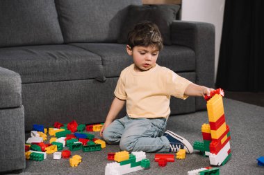 adorable toddler playing with colorful toy blocks while sitting on floor in living room  clipart