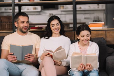 kanepede oturan ve oturma odasında ebeveynlerin yanında kitap okuma mutlu çocuk seçici odak 