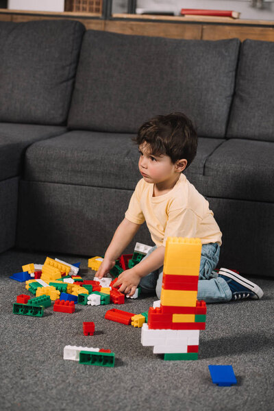 selective focus of cute toddler playing with colorful toy blocks in living room 