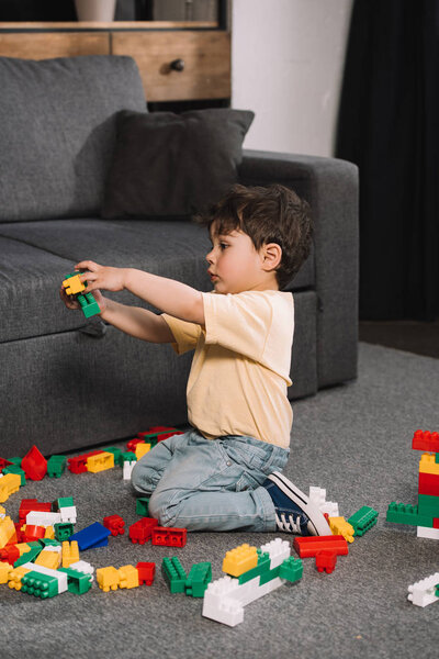 cute toddler playing with colorful toy blocks in living room 