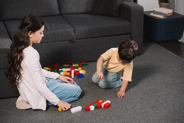 リビングルームでカラフルなおもちゃのブロックで遊ぶ幼児の弟を見てかわいい子供 — ストック写真