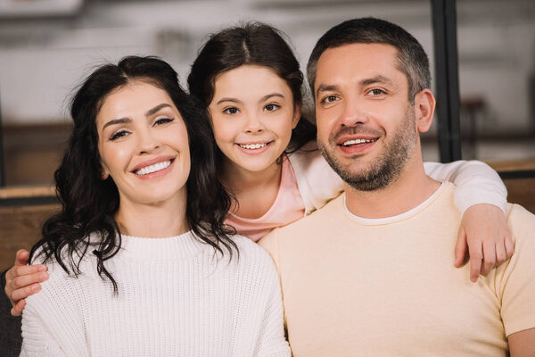 happy child and smiling parents looking at camera at home 