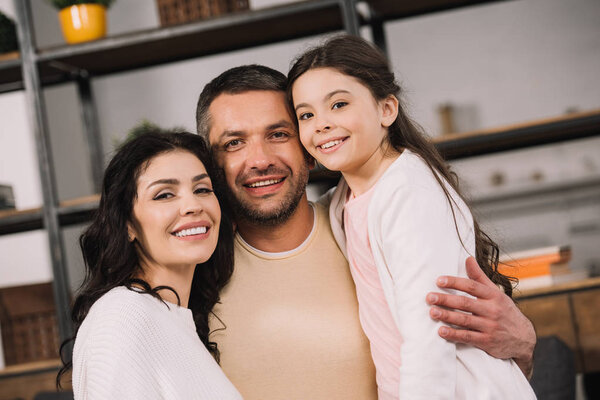 happy man hugging attractive wife and cute daughter at home 