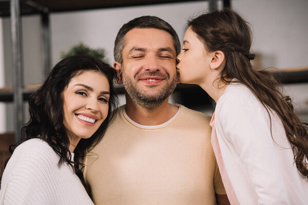cute daughter kissing cheek of happy father near attractive mother 