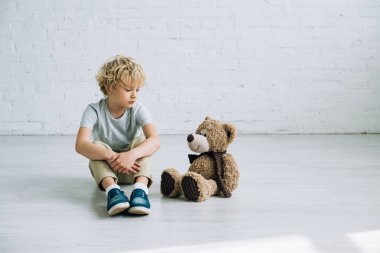 sad preteen boy with teddy bear sitting on floor clipart