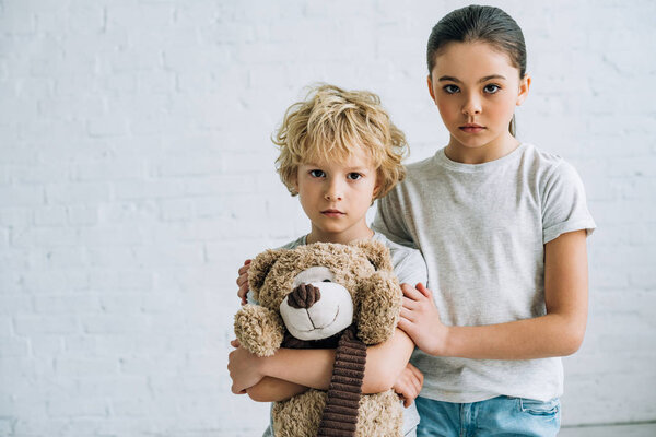 sad sister and brother with teddy bear at home