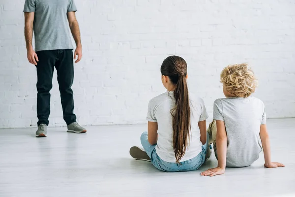 床に座っている虐待的な父親と悲しい子供たちの部分的なビュー — ストック写真