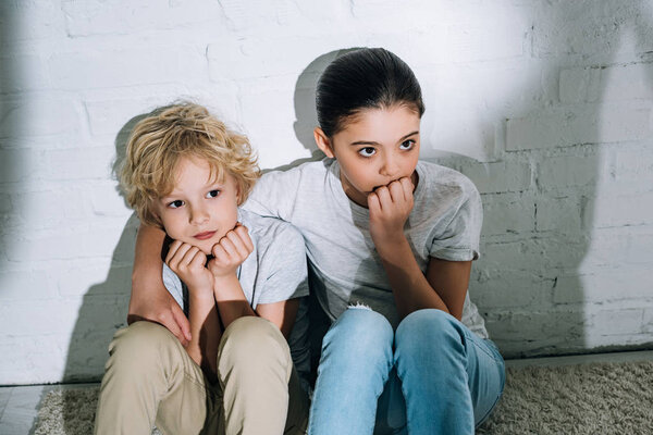 scared sister embracing brother while sitting on carpet