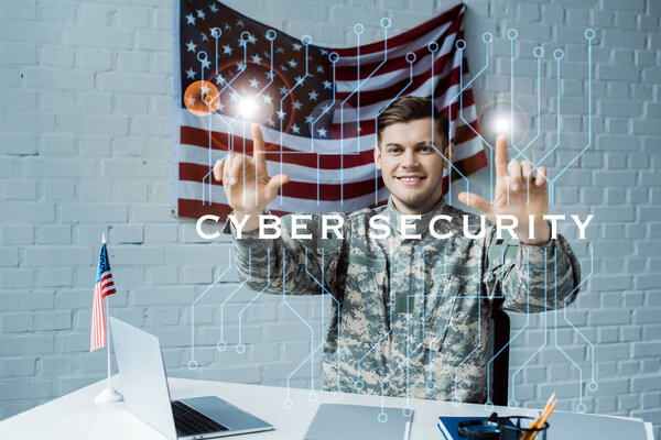 cheerful man in military uniform pointing with fingers at cyber security lettering