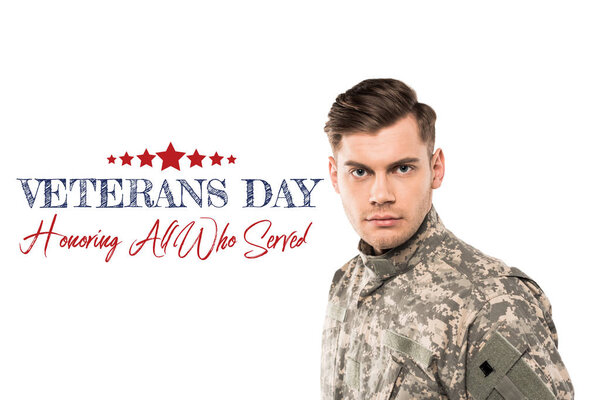 serious and handsome soldier in uniform looking at camera near veterans day lettering on white 