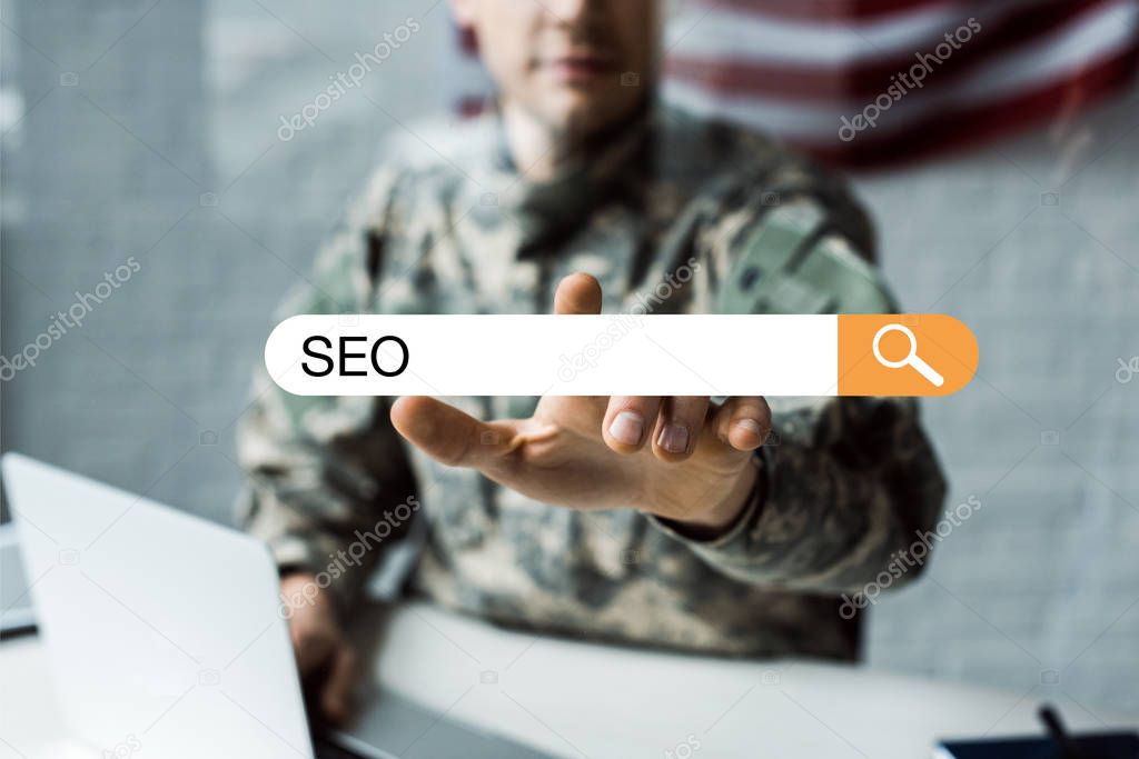selective focus of man in military uniform pointing with finger at address bar with seo lettering 