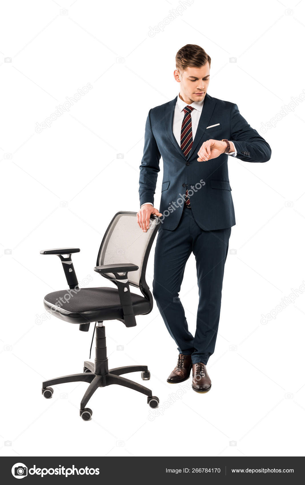 confident businessman standing near chair and looking at watch isolated on  white 266784170
