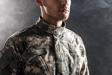 cropped view of serious soldier in military uniform on black with smoke  clipart