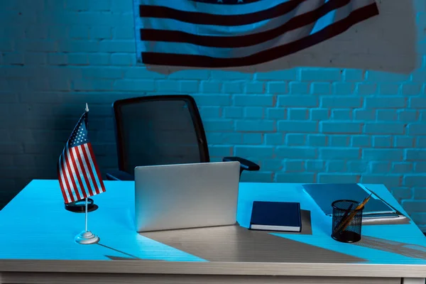 laptop near stationery near american flag in modern office