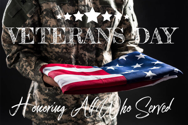 cropped view of soldier in military uniform holding flag of america near veterans day lettering on grey 